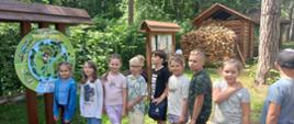 Grupa dzieci stoi w lesie przed tablicą informacyjną