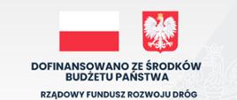 Na szaro- białym tle z flagą i godłem Polski tablica informacyjna- inwestycja dofinansowana ze środków budżetu- Rządowy Fundusz Rozwoju Dróg: przebudowa odcinka drogi powiatowej w zakresie przebudowy istniejącej zatoki autobusowej relacji Proszowice–Koszyce w m. Stogniowice, gm. Proszowice oraz relacji Proszowice- Koszyce w m. Koszyce, gm. Koszyce.
