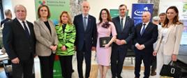 Wspólne zdjęcie gości i organizatorów na tle banerów KRUS i Mlekpol. W centrum Dyrektor Karolina Ilczuk w różowej sukience oraz Minister Stefan Krajewski, Senator Marek Adam Komorowski i Wójt Jarosław Kos.
