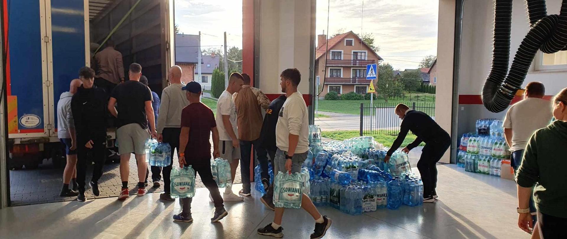 mężczyźni i kobiety ładują zgrzewki wody na tira 