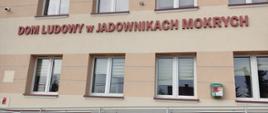 Budynek Domu Ludowego w Jadownikach Mokrych z widocznym napisem na ścianie, szeregiem okien oraz podjazdem dla osób z niepełnosprawnościami.