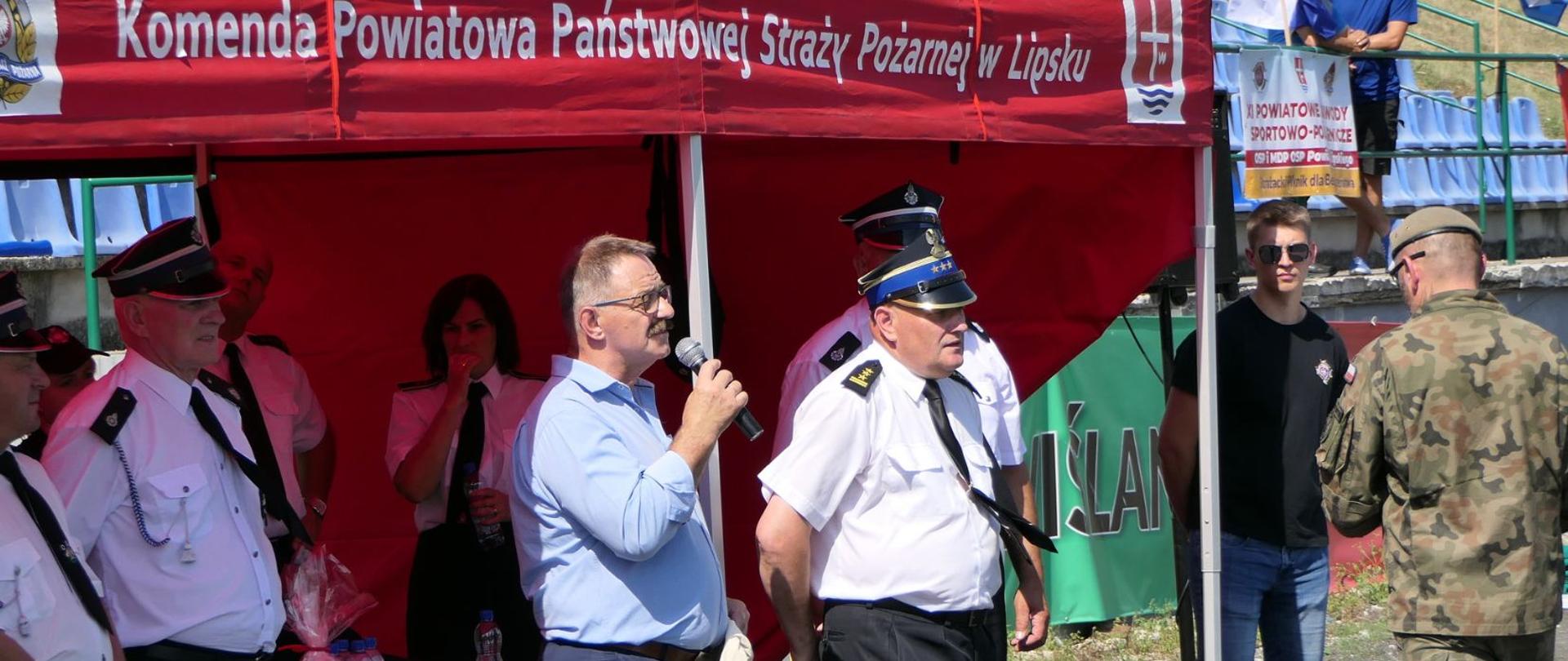 Przemówienie Starosty Lipskiego przed ogłoszeniami wyników. Po jego prawej stronie stoi Komendant Państwowej Straży w Lipsku - Tomasz Krzyczkowski. W tle pod namiotem znajdują się pozostali zaproszeni goście.