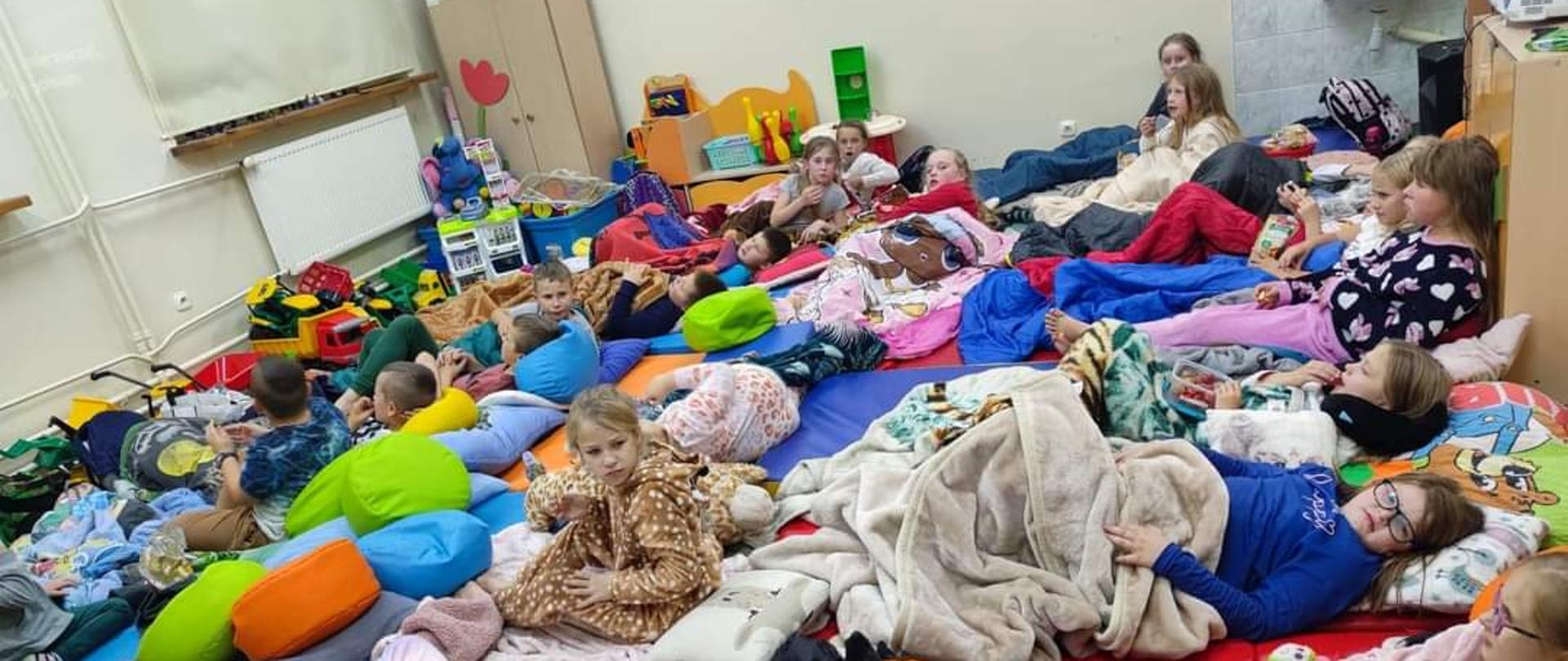 Zdjęcia przedstawia przygotowania do noclegu w szkole, w klasie. Cała klasa w śpiworach a na nich zuchy , których czeka nocleg w tej klasie..