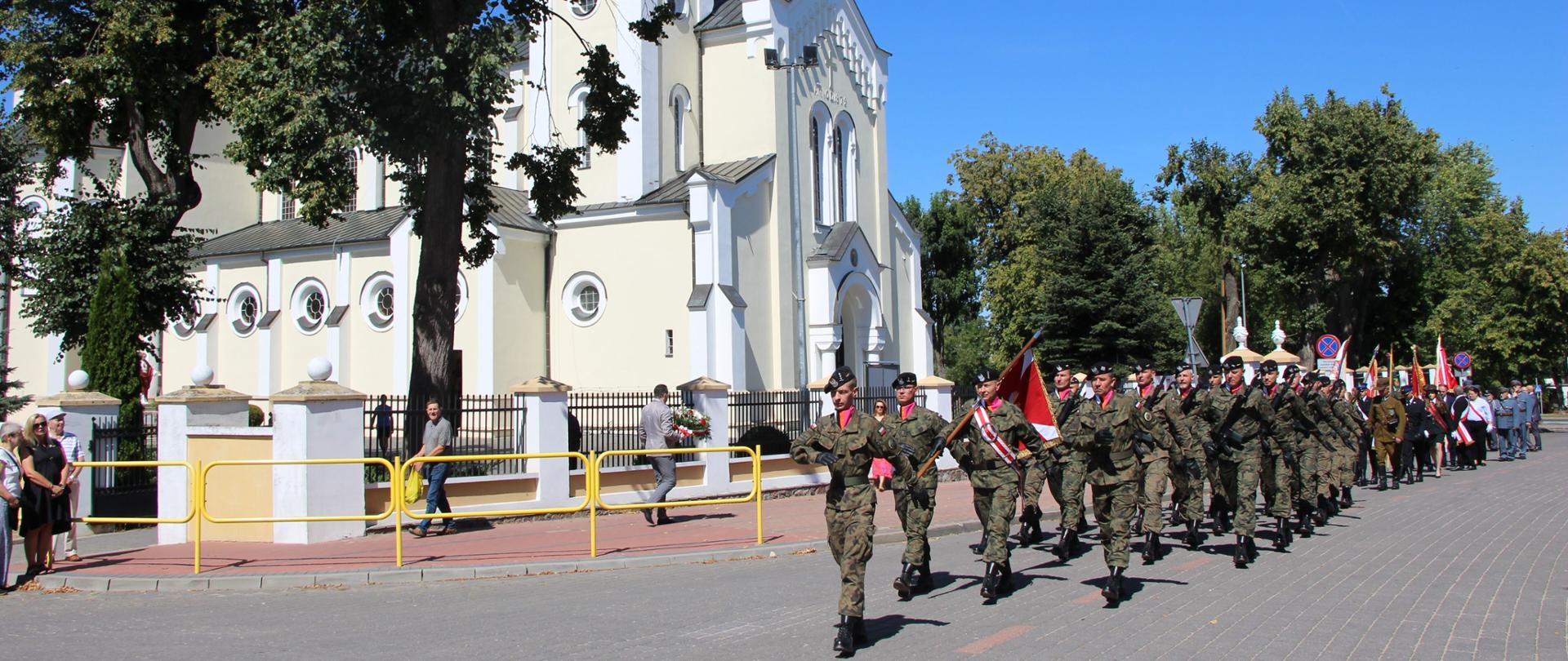 Kompania reprezentacyjna 2. Brygady Pancernej Legionów z Czerwonego Boru maszeruje ulicą w Zambrowie podczas obchodów Święta Wojska Polskiego. W tle widoczny kościół pw. Trójcy Przenajświętszej.