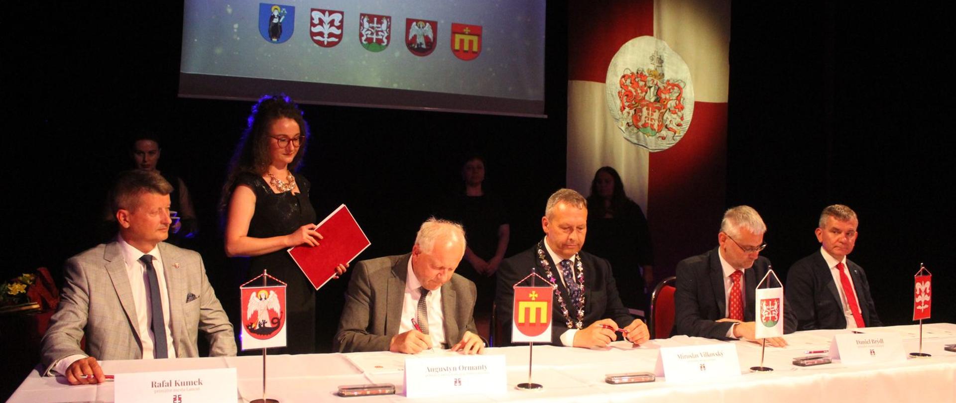 Moment podpisania umowy partnerskiej, przy stole siedzą mężczyźni. 