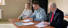 Dwóch mężczyzn podpisujących umowę, obok siedzi kobieta i mężczyzna.