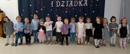 Dzieci w trakcie części artystycznej uroczystości - stoją w rzędzie, recytują i śpiewają.