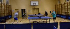 Uczestnicy rozgrywają mecz - widok trzech stołów do tenisa stołowego i grające dwuosobowe drużyny
