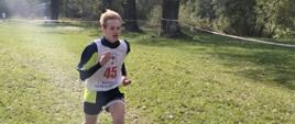 Uczeń w koszulce z numerem 45 biegnie z rozwianym włosem na trasie trawiastej, w tle widoczne drzewa