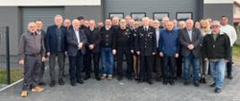 Grupa osób stojących obok siebie przed budynkiem remizy OSP Prosna