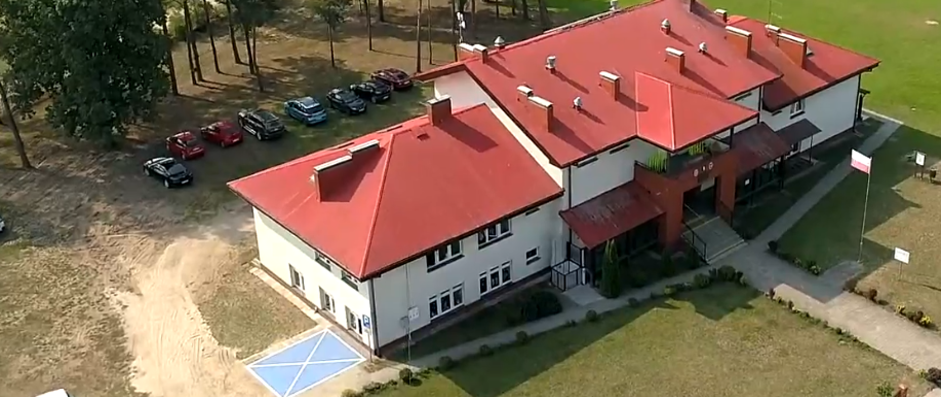 Budynek Szkoły Podstawowej w Holonkach z "lotu ptaka"Na zdjęciu widoczny zewnętrzny fragment platformy schodowej oraz miejsce parkingowe dla osoby niepełnosprawnej.