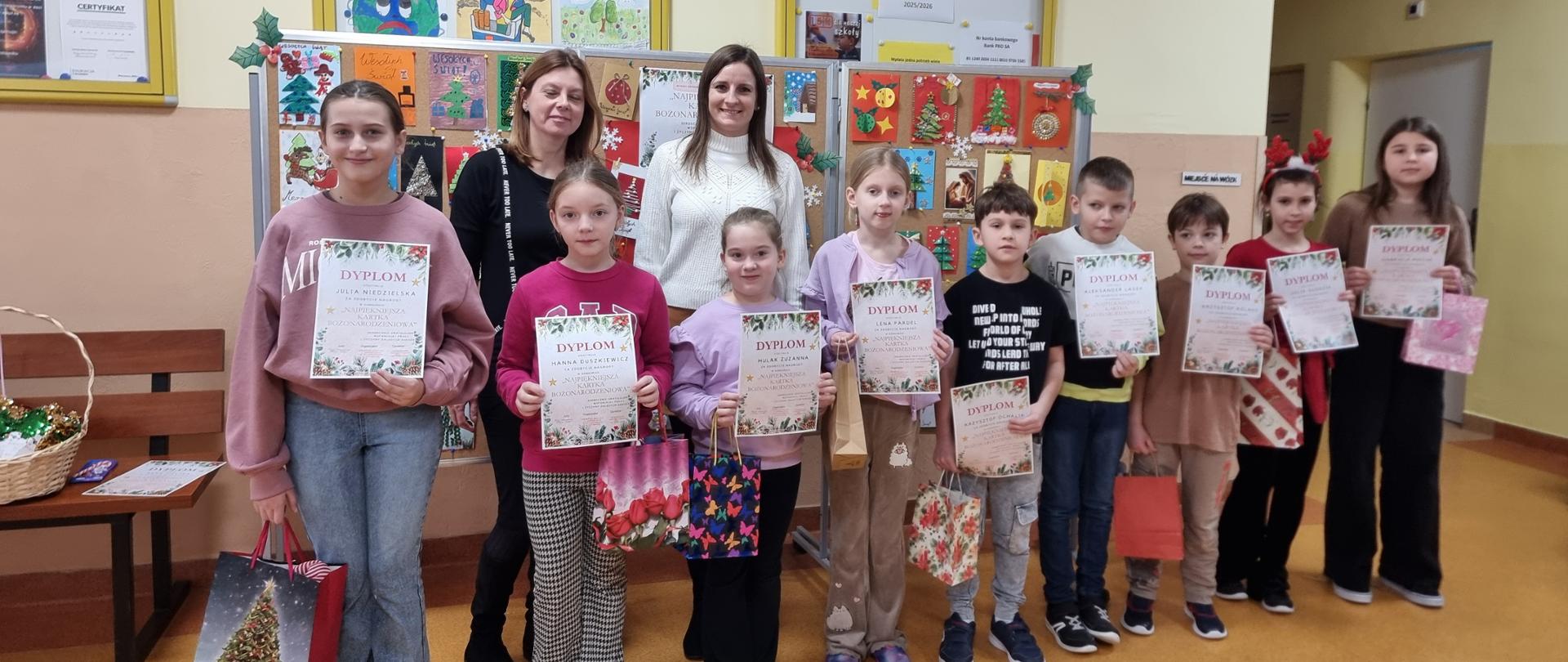 Laureaci konkursu z dyrekcją szkoły ustawieni na tle tablicy prezentującej wykonane prace.