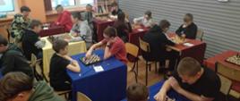 Sala ze stolikami, przy których uczniowie grają w szachy
