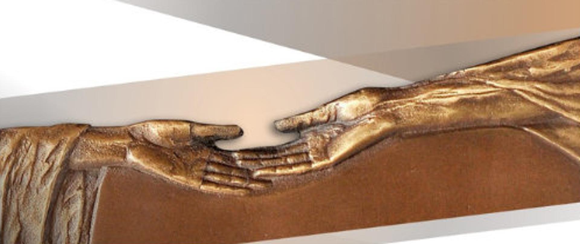 Na biało-beżowo-brązowym tle napis Nagroda Amicus Hominum, pod spodem fragment płaskorzeźby z dwoma stykającymi się, otwartymi do góry dłońmi