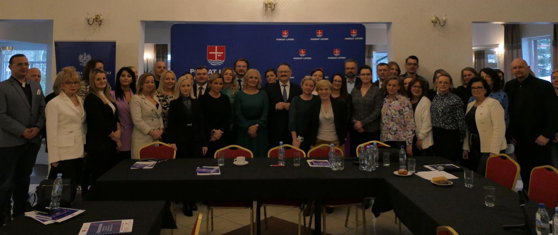 Wszyscy uczestnicy Konwentu pozują do zdjęcia. W tle granatowa ścianka z herbem powiatu.