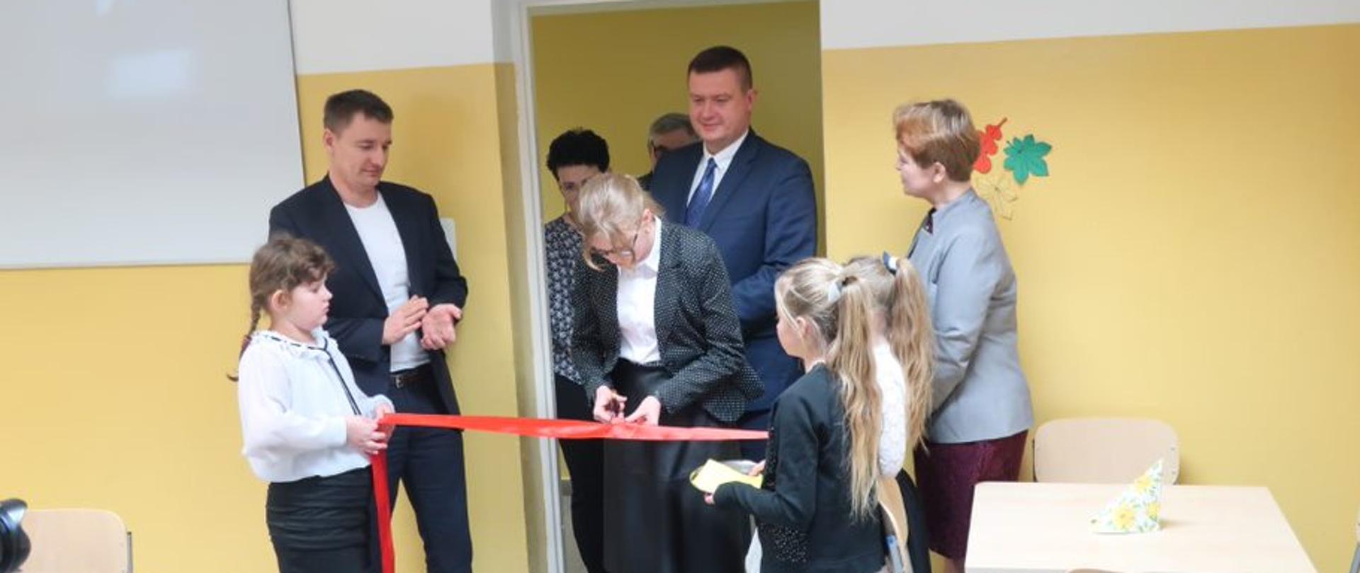 Uroczystość przecinania wstęgi w pomieszczeniu stołówki, uczestniczy w nim 9 osób