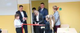 Uroczystość przecinania wstęgi w pomieszczeniu stołówki, uczestniczy w nim 9 osób