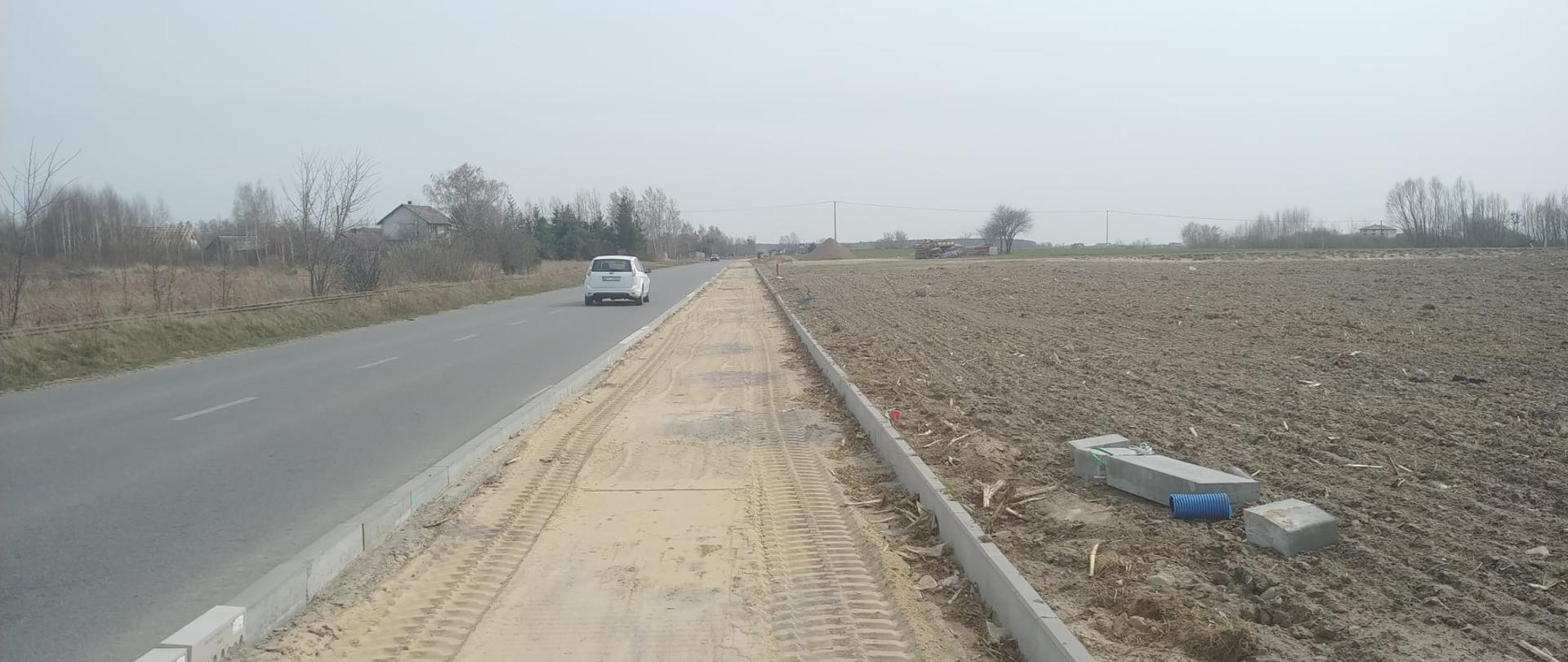 Zdjęcie przedstawia fragment budowy ścieżki pieszo-rowerowej biegnącej wzdłuż asfaltowej drogi biegnącej z Przasnysza do Leszna i Gostkowa.