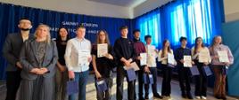 Troje dorosłych i grupa dzieci. Dzieci trzymają w jednym ręku kartki z napisem dyplom a w drogiej granatową papierową torebkę
