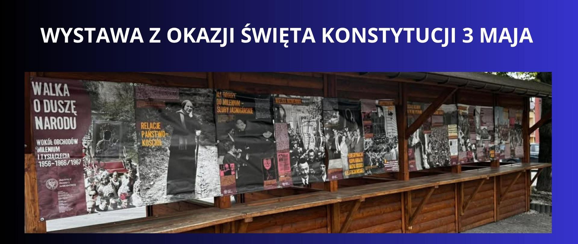 BIAŁY NAPIS NA GRANATOWO CZARNYM TLE "WYSTAWA Z OKAZJI ŚWIĘTA KONSTYTUCJI 3 MAJA " ZDJĘCIE WYSTAWY NA RYNKU 
