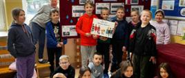 Uczniowie stoją na tle gazetki informacyjnej na temat wody z plakatami i niebieskimi kropelkami wody, dwóch uczniów na środku trzyma plakat z logo programu "Aktywni Błękitni"