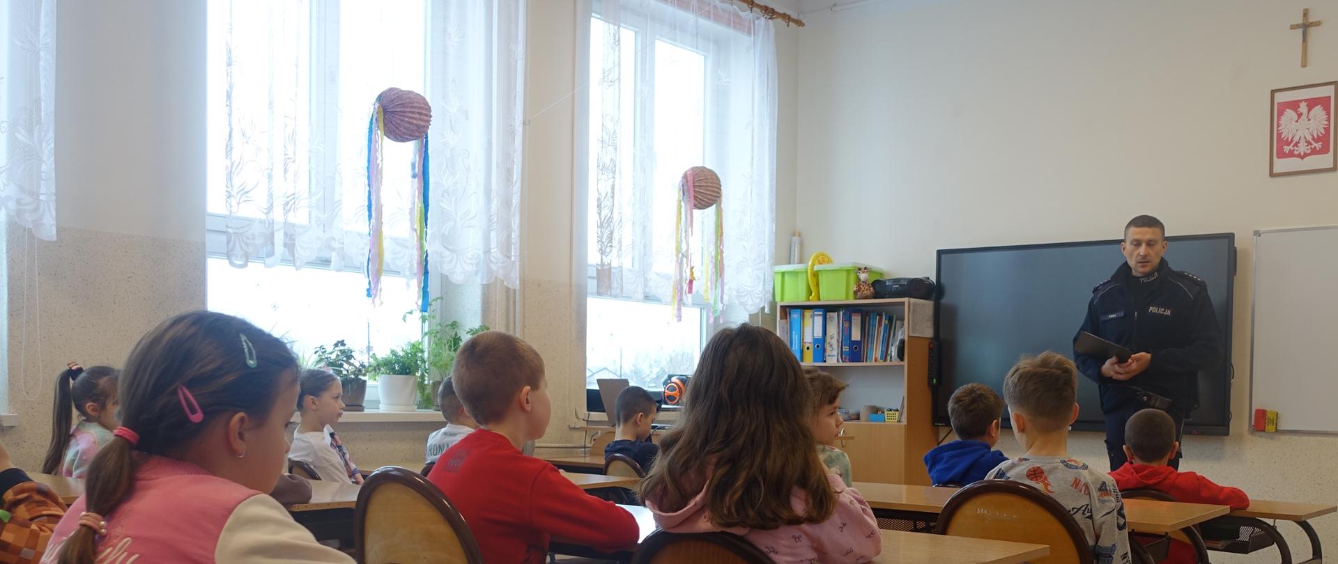 Uczniowie w sali lekcyjnej uczestniczą w prelekcji policjanta