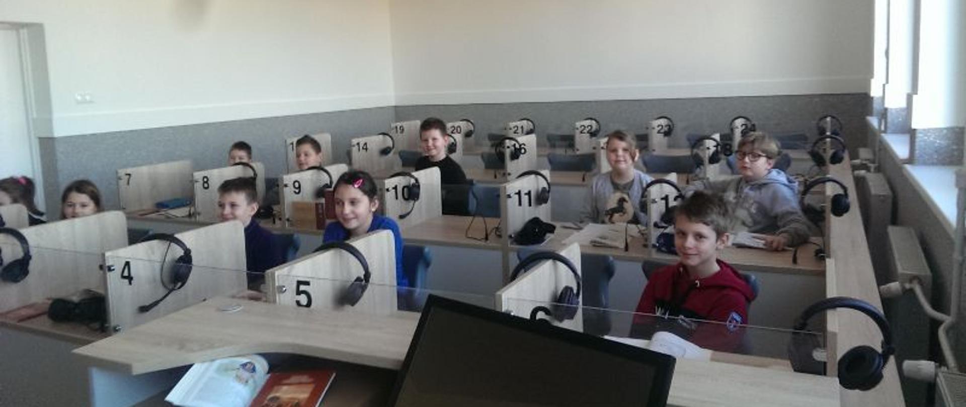 Zdjęcie przedstawia nowoczesną pracownie językową w Zespole Szkół w Lutocinie. Są w niej dzieci, które korzystają z nowej sali podczas lekcji.