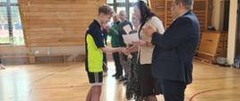 Uczeń naszej szkoły w granatowo-żółtym stroju sport owym odbiera puchar i dyplom od pani wójt gminy Łabowa w towarzystwie nauczycieli wychowania fizycznego drużyn przeciwnych