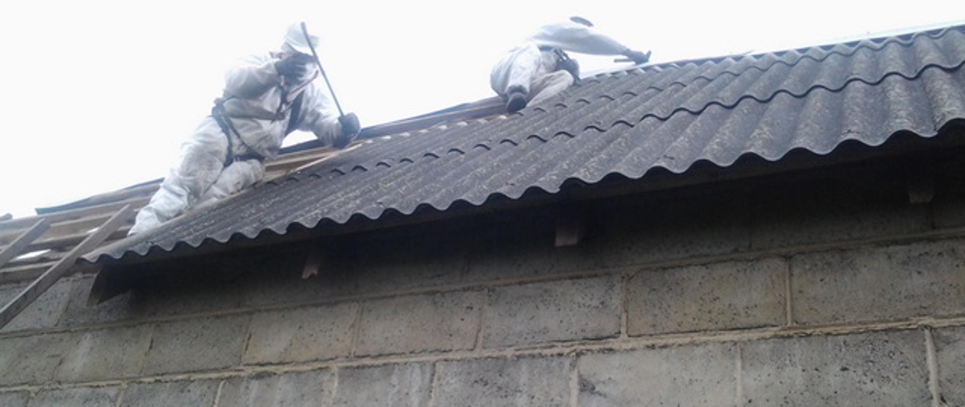 dwóch pracowników na dachu demontujących płyty azbestowe faliste na budynku mieszkalnym