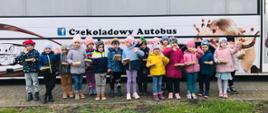 Dzieci stoją przed Czekoladowym Autobusem z pudełeczkami wypełnionymi czekoladkami, które zrobiły podczas warsztatów
