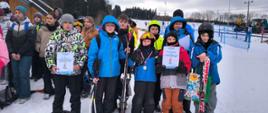 Uczniowie pozują do zdjęcia na stoku z medalami, dyplomami i nartami