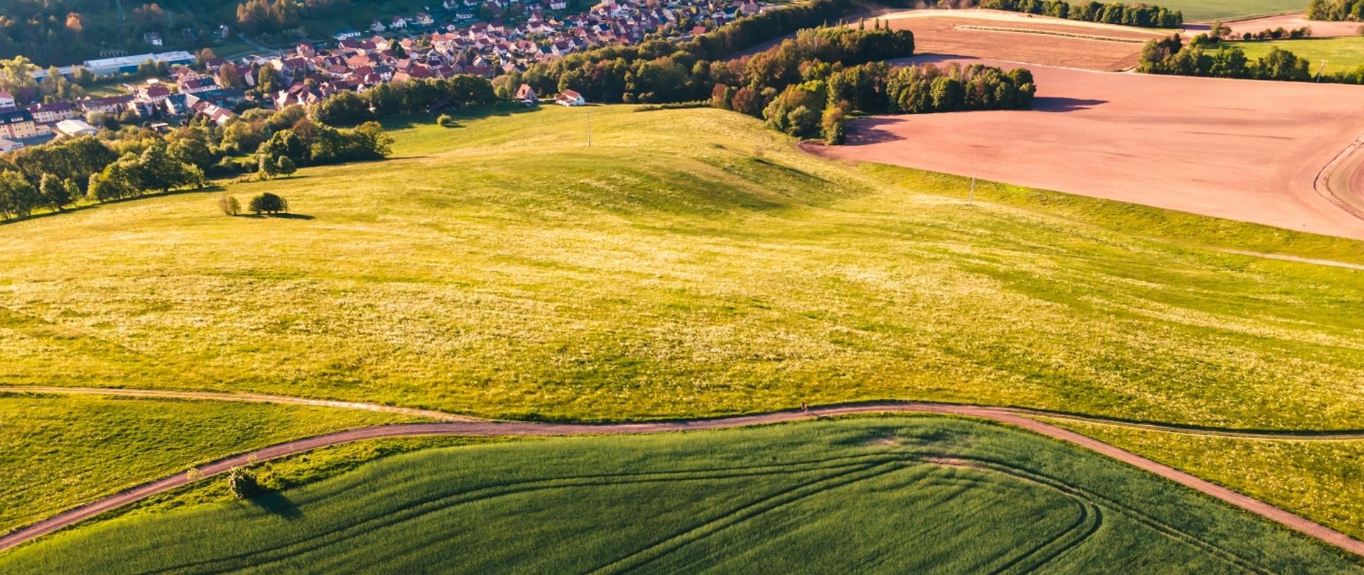Widok z lotu ptaka na zielone pola uprawne oraz wioskę w dolinie.