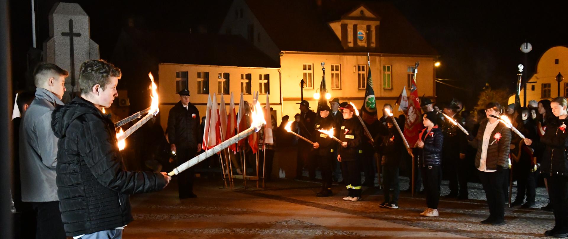 ludzie z pochodniami i sztandarami zgromadzeni na Rynku w Margoninie podczas obchodów Święta Niedpodległości