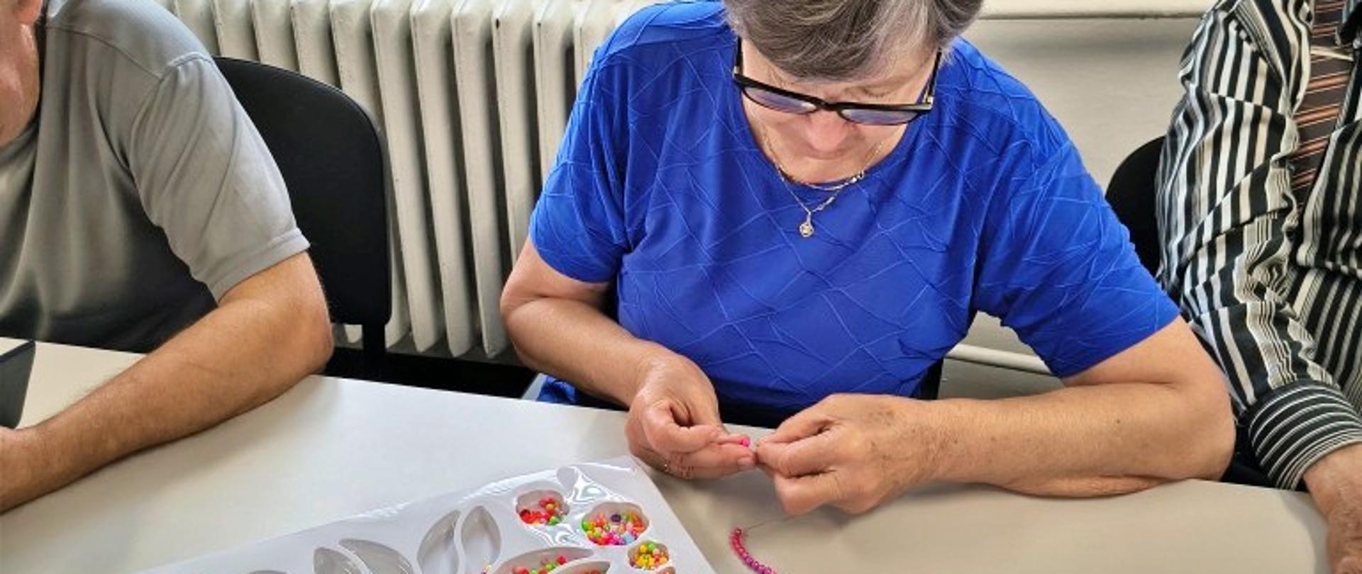 seniorzy podczas zajęć wykonują bransoletki z koralików