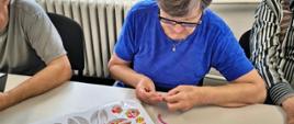seniorzy podczas zajęć wykonują bransoletki z koralików