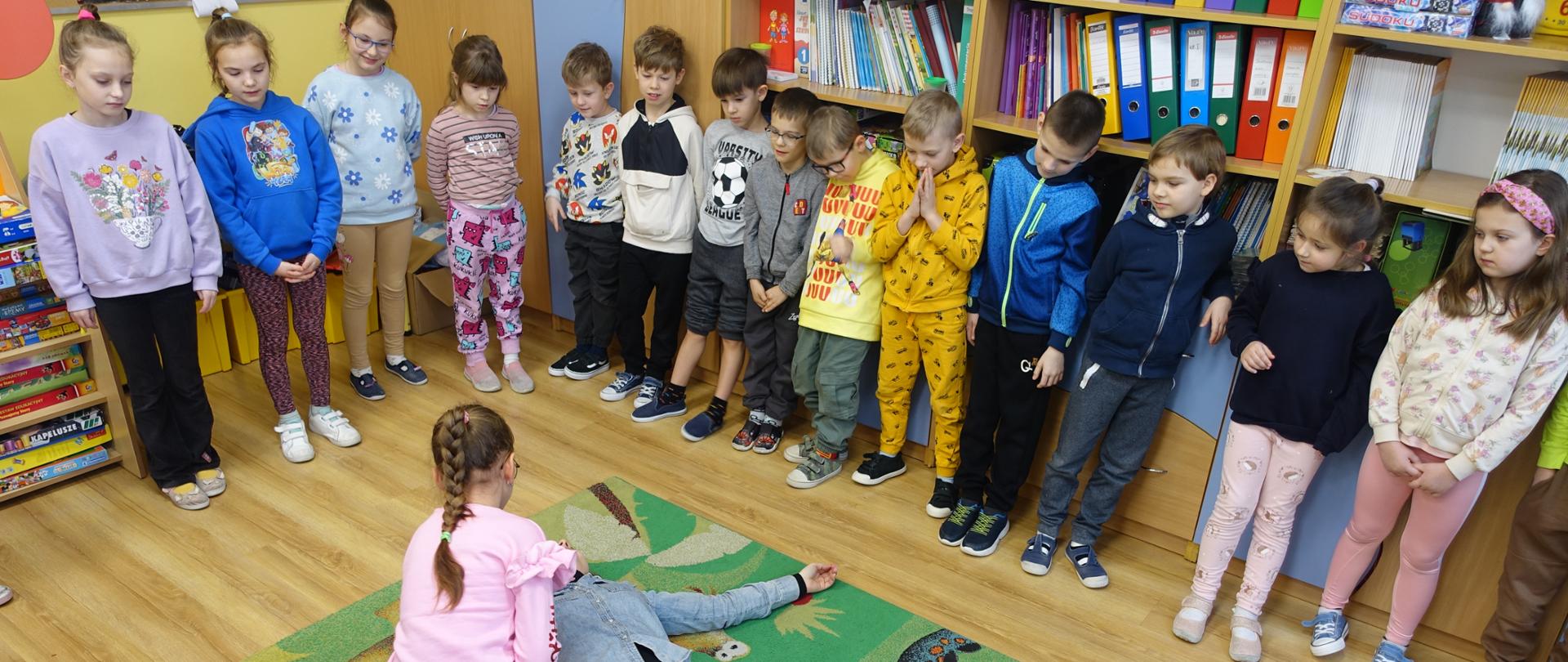 Uczennica układa osobę poszkodowaną w pozycji bocznej ustalonej.