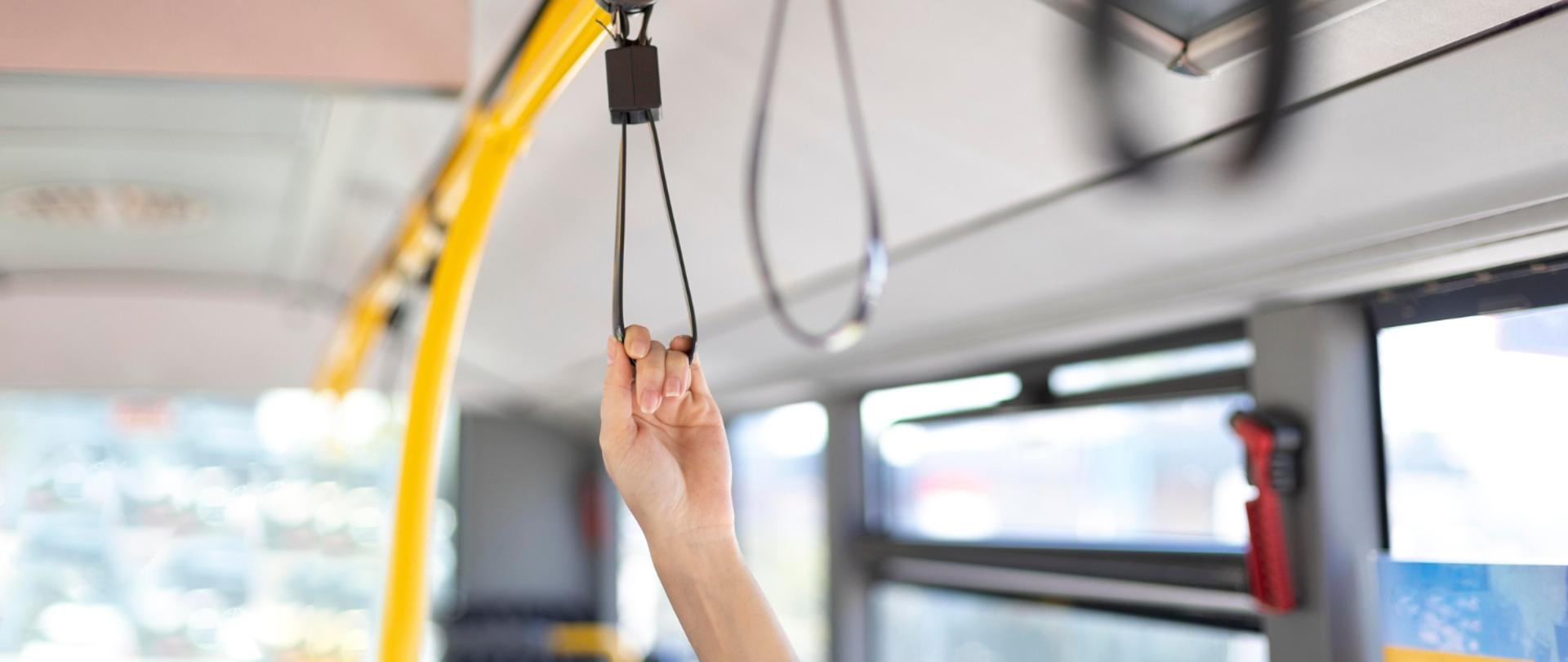 Wnętrze autobusu. Widać kobiecą rękę trzymającą poręcz.
