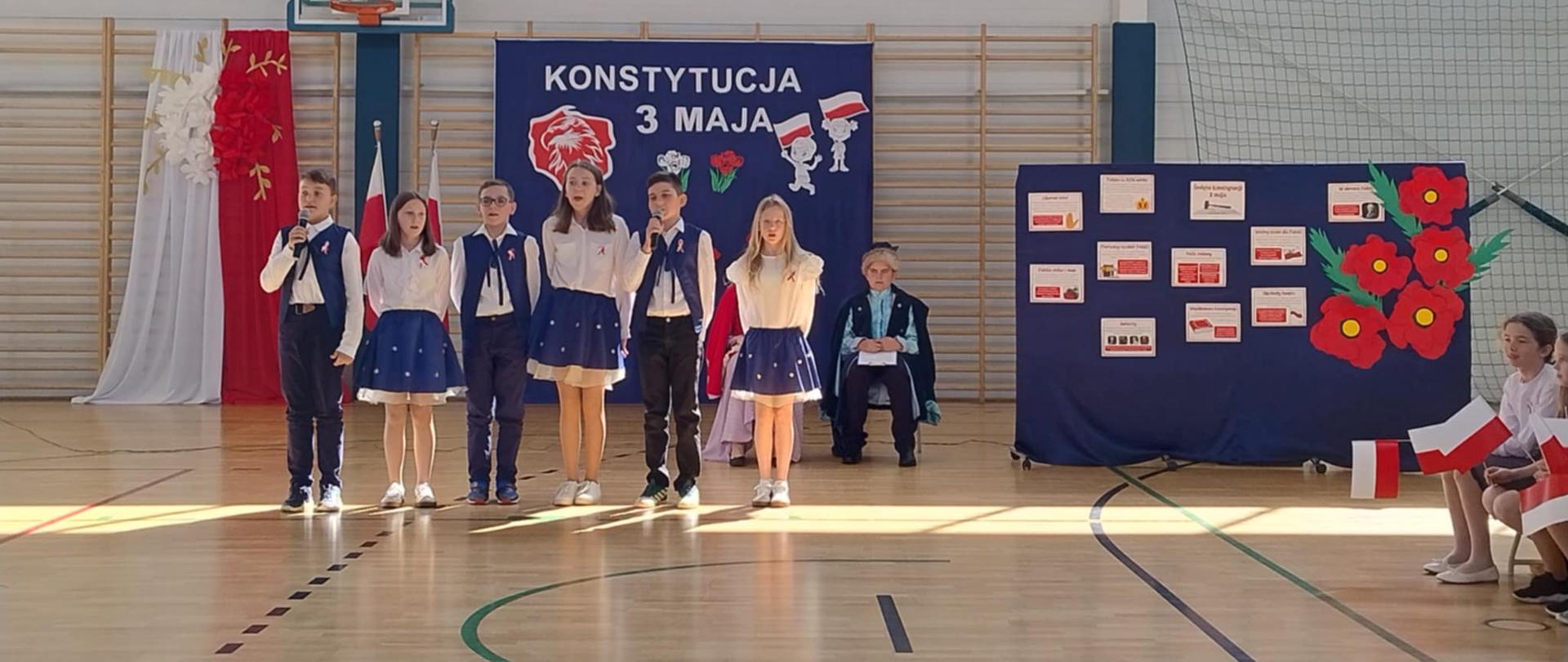 Na pierwszym planie uczniowie klasy IV w trakcie występu na tle dekoracji 