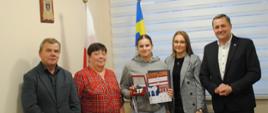 Radni i Wójt Gminy Raba Wyżna oraz zawodniczka Martyna Gacek stoją w gabinecie Wójta. Dziewczyna w rękach trzyma dyplom oraz medal. W tle widać dwie flagi