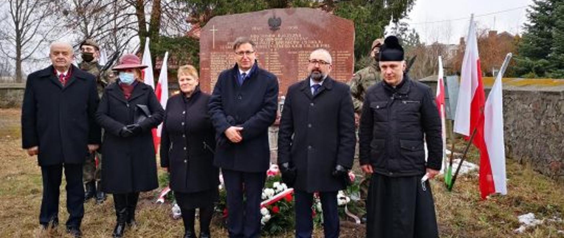 Zdjęcie przedstawia od lewej: Zastępcę Głównego Inspektora Ochrony Roślin i Nasiennictwa w Warszawie – Tadeusza Łączyńskiego, Poseł na Sejm Rzeczypospolitej Annę Cicholska, Przedstawicielka rodzin poległych żołnierzy, Prezes Instytutu Pamięci Narodowej dr Jarosław Szarek, Starosta Powiatu Przasnyskiego Krzysztof Bieńkowski, Proboszcz parafii w Zielonej ksiądz Andrzej Gajewski. W tle pomnik pomordowanych i poległych w walkach żołnierzy wyklętych oraz żołnierze pełniący wartę honorową.