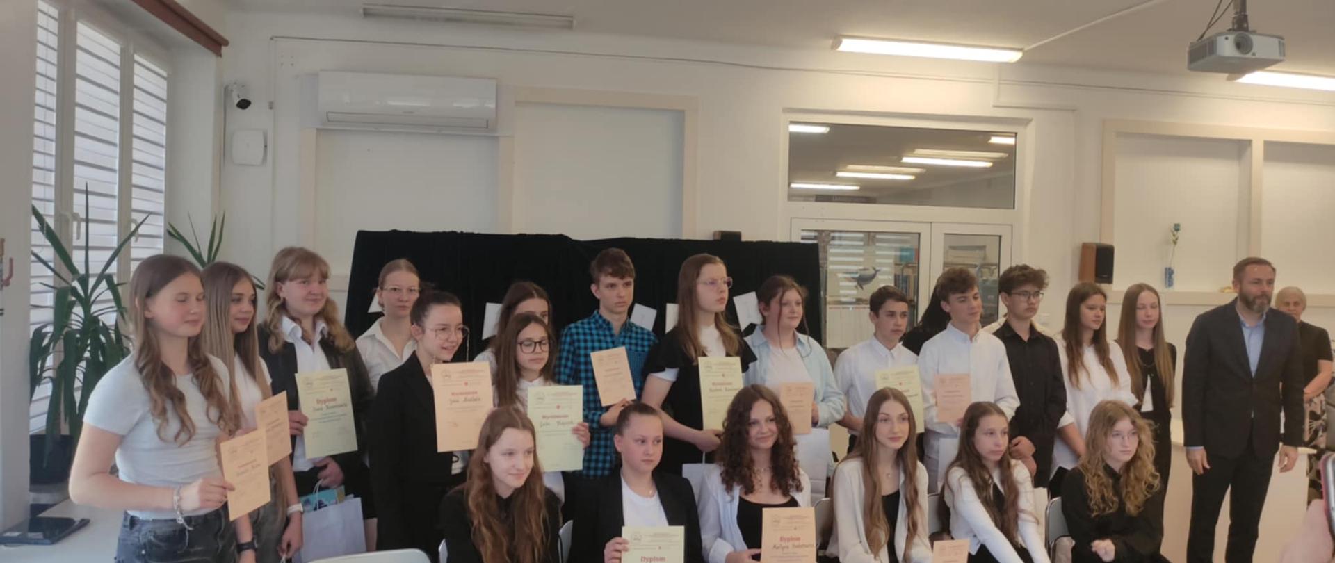 Grupa uczniów biorących udział w konkursie recytatorskim trzyma w dłoniach dyplomy i pozuje do wspólnego zdjęcia.