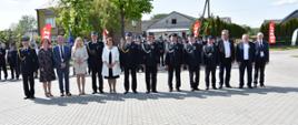 Zdjęcie grupowe na placu z betonowej kostki brukowej. Na fotografii dowództwo jednostki OSP Błonie Duże, zaproszeni goście, osoby odznaczone medalami. W tle poczty sztandarowe.