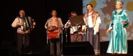 Zespół w strojach ludowych i muzykami na scenie