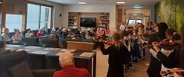 Dzieci z instrumentami muzycznymi grają dla starszych osób siedzących na dużej sali