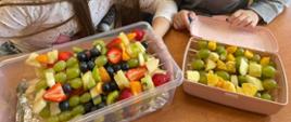 Dwa pojemniki z nabitymi na patyczek do szaszłyki owocami: banan, truskawka, winogrona, pomarańcza