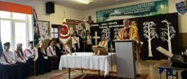 Na głównym korytarzu szkolnym odbywa się Msza Święta. Na środku stoi ołtarz oraz mównica przy której stoi ksiądz. Obok ołtarza siedzą uczniowie reprezentujący sztandary szkolne.