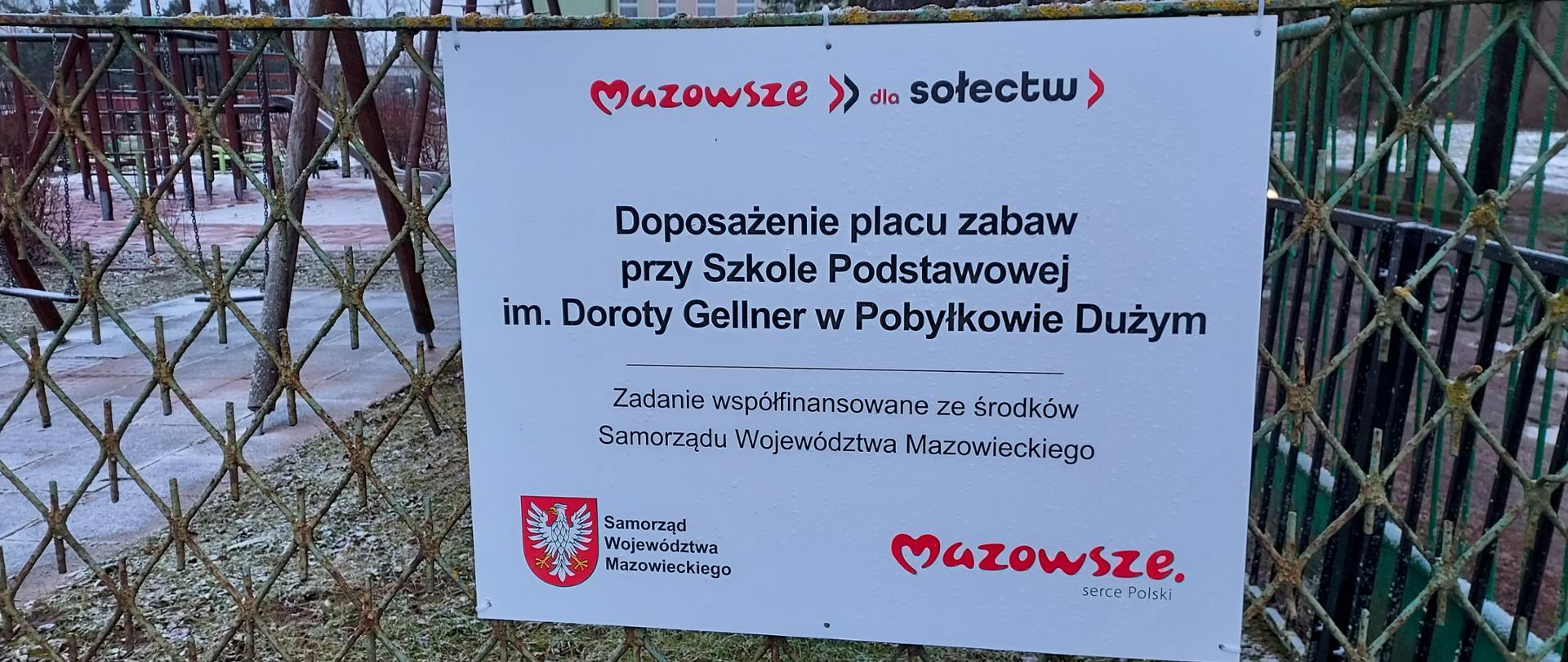 Zdjęcie przedstawia tablicę informacyjną o treści: Doposażenie placu zabaw przy Szkole Podstawowej im. Doroty Gellner w Pobyłkowie Dużym - zadanie współfinansowane ze środków Samorządu Województwa Mazowieckiego. Na zdjęciu umieszczono logo marki Mazowsze oraz logo programu "Mazowsze dla sołectw"