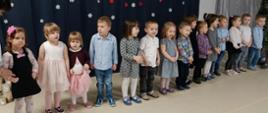Dzieci w trakcie części artystycznej uroczystości - stoją w rzędzie, recytują i śpiewają.