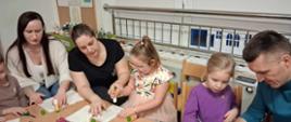 Rodzice z dziećmi siedzą przy stole, przygotowują gwiazdy z papieru