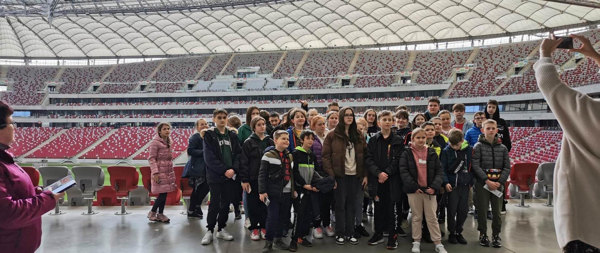 Uczniowie uczestnicy wycieczki do Warszawy na Stadionie Narodowym, w tle trybuny i zielona murawa
